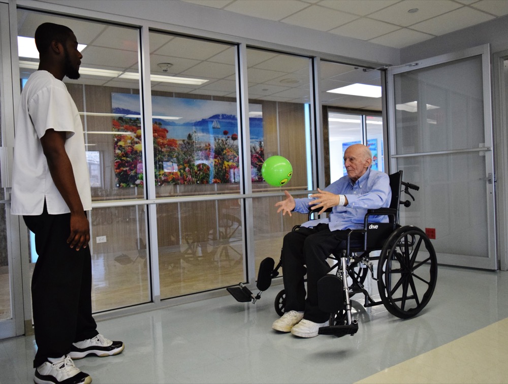 Man catching a therapy ball from therapist while sitting in wheelchair